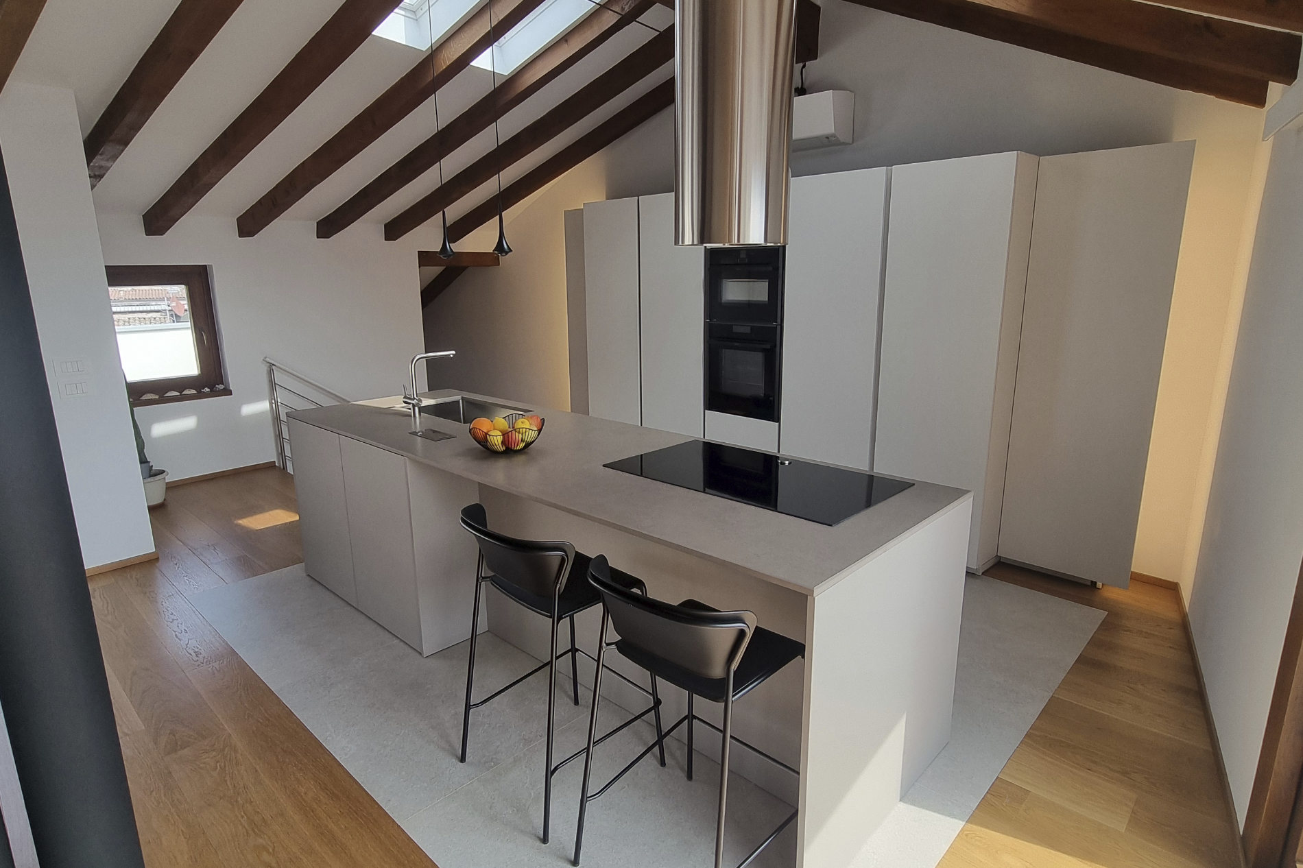 foto di una cucina con penisola e piano induzione e lavello al suo interno di colore grigio, davanti alla penisola 2 sedute alte in ferro color nero